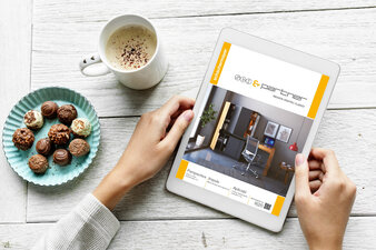 Doamna vizioneaza revista SCH&Partner pe tableta alaturi cu cafea si bomboane