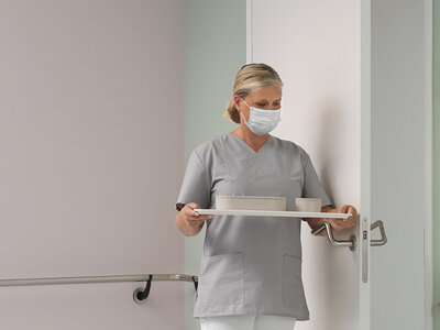 Maner antibacterian FSB pentru deschiderea cu antebratul Asistenta medicala cu tava in mana deschide usa cu antebratul, apasand pe manerul anticovid.